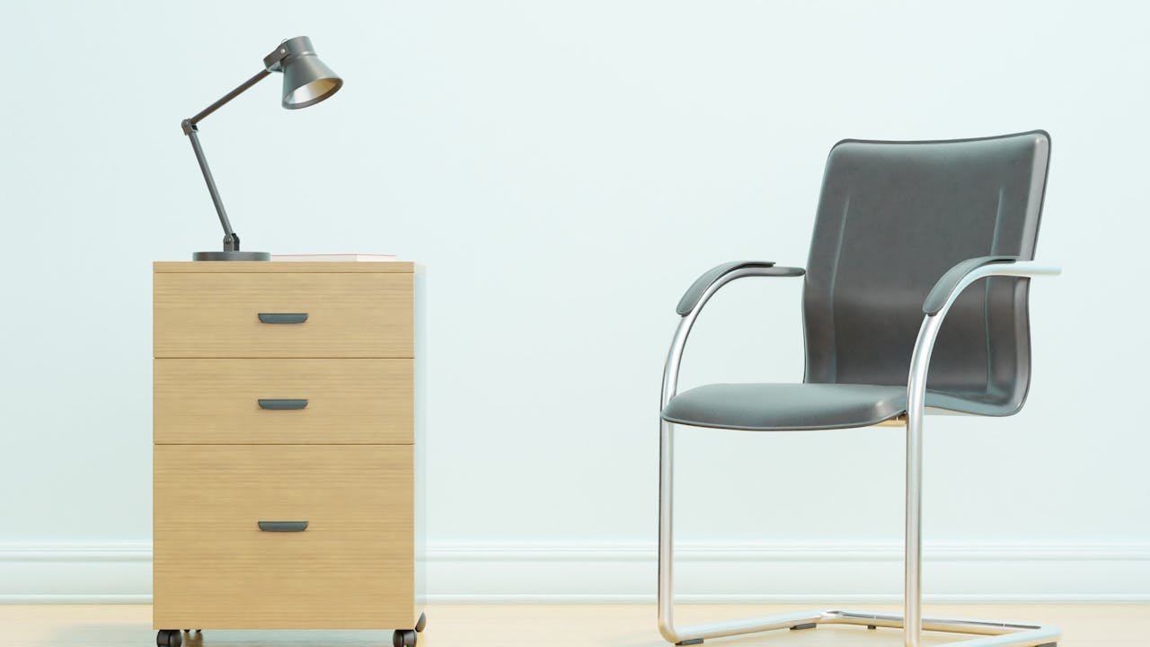 hero-img-01 A minimalist office setup showcasing a sleek chair and wooden drawer unit with a desk lamp.